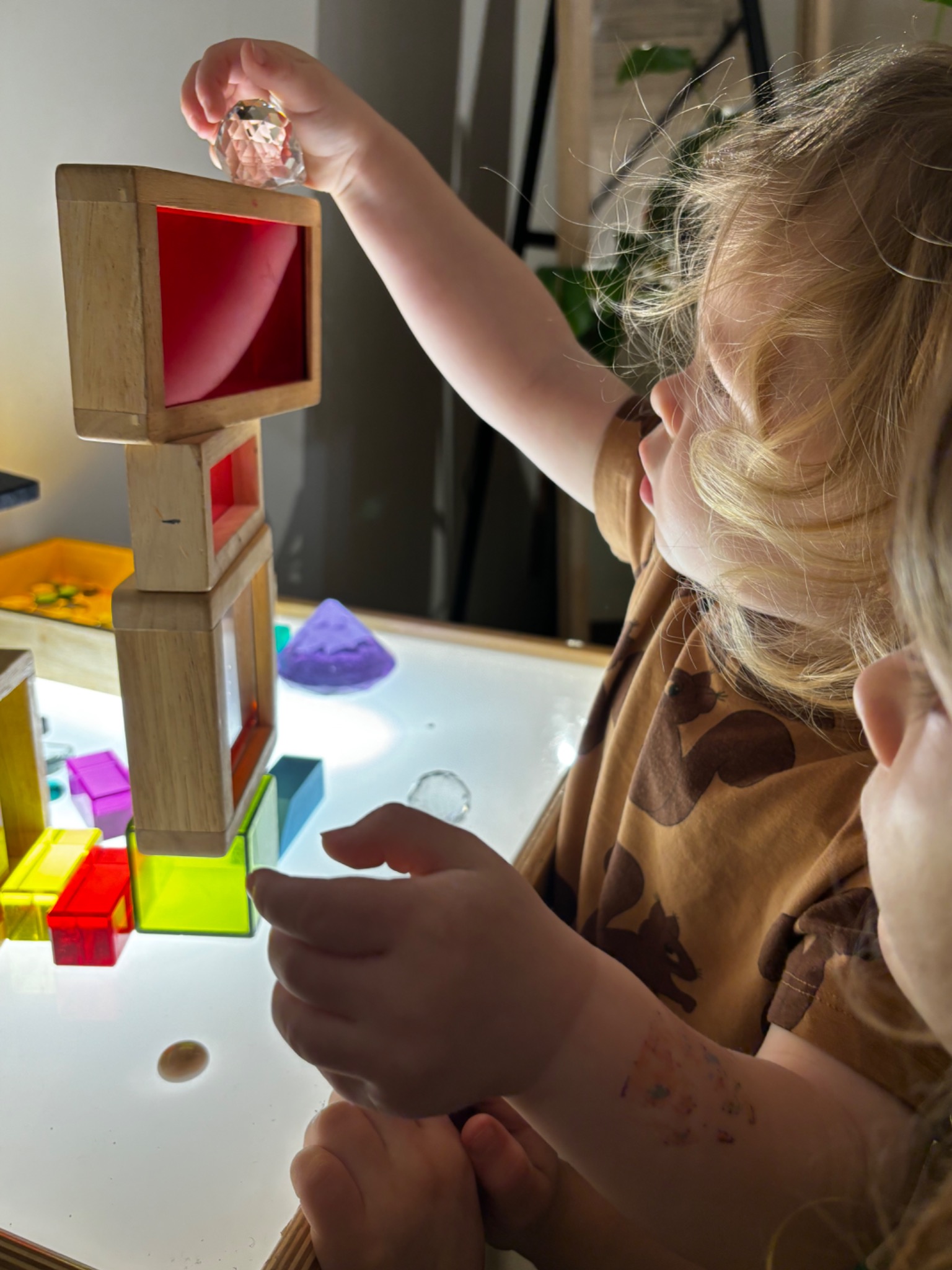 A child carefully stacking colorful wooden blocks on a light table
