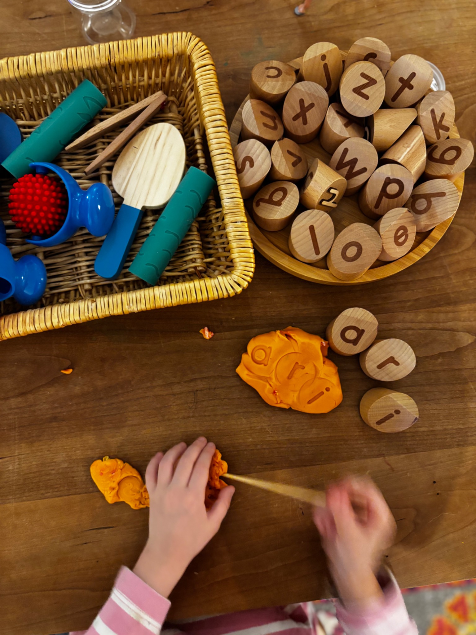 A child exploring orange play dough with wooden letter stamps
